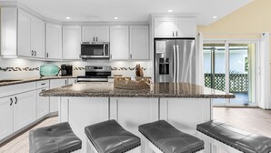 A modern kitchen with white cabinets, a granite countertop, stainless steel appliances, and a bar area with leather stools.