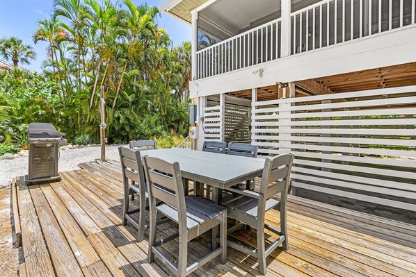 A wooden deck with a table and chairs, a grill, and a white railing.