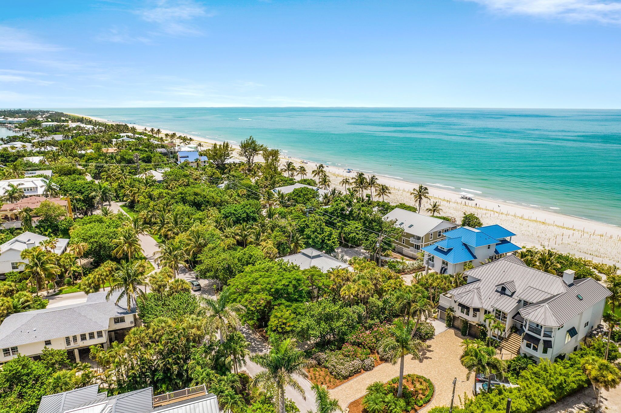 An aerial view of a coastal residential area with houses, a beach, and a clear blue sky.