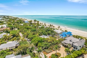 An aerial view of a coastal residential area with houses, a beach, and a clear blue sky.