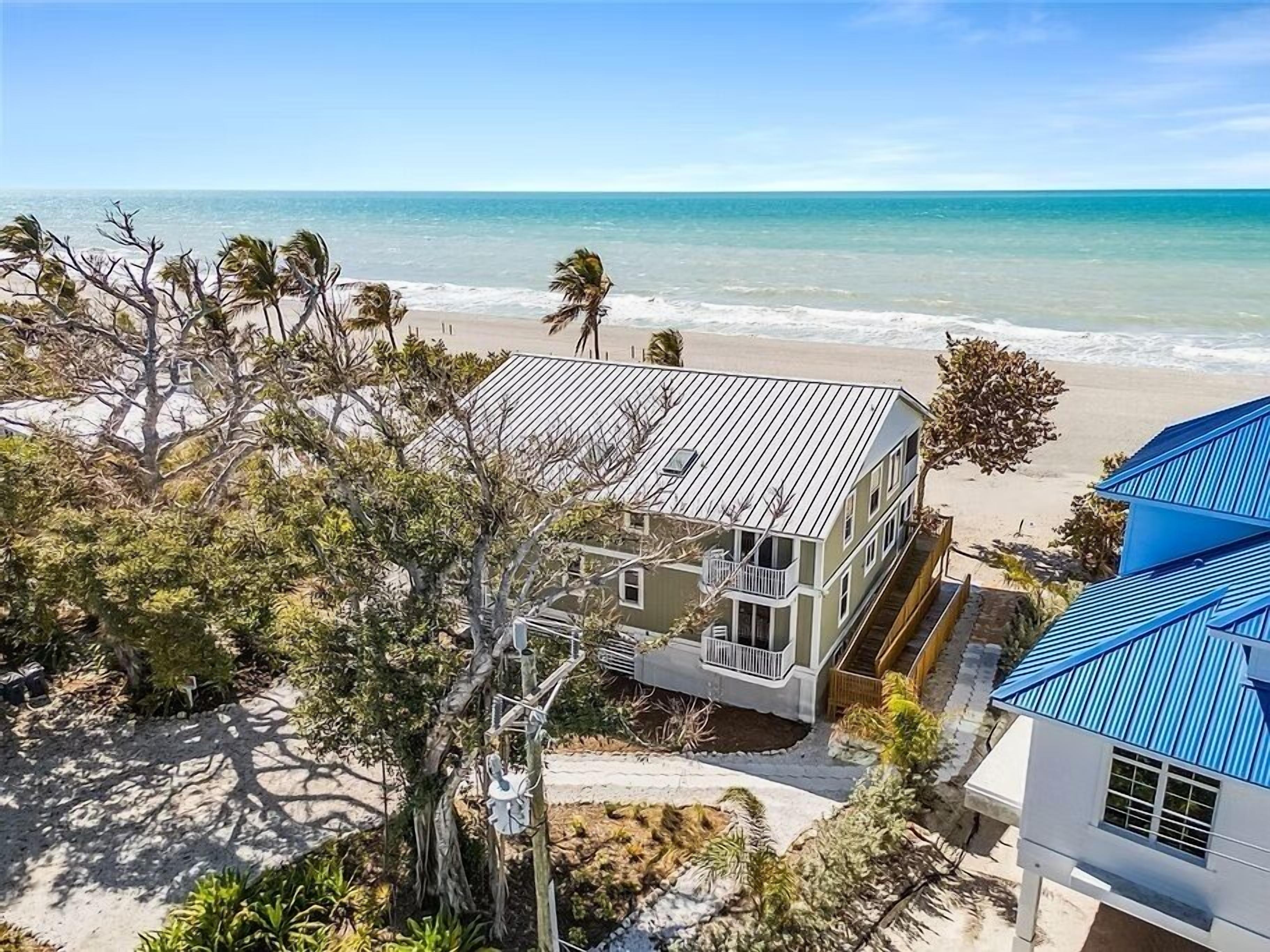 Une propriété située en bord de mer, comprenant une grande maison, un bâtiment plus petit et une construction surmontée d’un toit bleu.