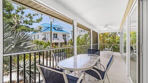 A balcony with a glass table and chairs, a view of a house with a blue roof, and a palm tree. - Modern 2-Bedroom Retreat Steps from Captiva Beach (Captiva)