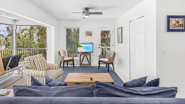 A sunlit living room with a sofa, chairs, a coffee table, and a TV.