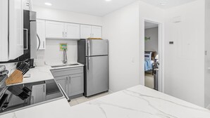 A modern kitchen with white cabinetry, a stainless steel refrigerator, and a marble countertop.