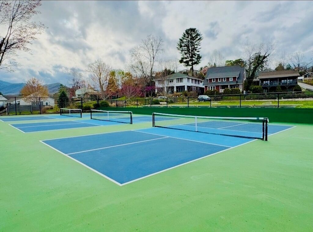 An outdoor tennis court with a net, surrounded by houses and trees.