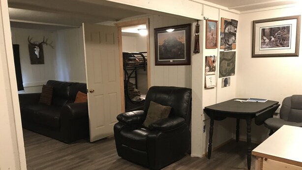 A room with a black leather chair, a small table, and a couch. There are framed pictures on the wall and a door leading to another room.
