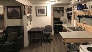 A compact kitchen with a sink, stove, and dining area. There are framed pictures on the wall and a fan near the kitchen.
