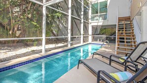 An indoor swimming pool with clear blue tiles, surrounded by a glass enclosure with a view of tropical foliage.