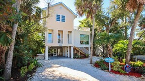 A two-story house with a covered porch, palm trees, and a sign indicating 'Sea Breeze'.