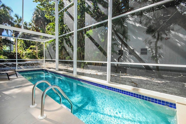 A swimming pool with clear blue water, surrounded by a white fence and palm trees.