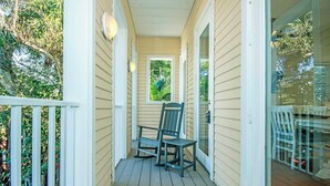 A covered porch with a wooden floor, a rocking chair, and a table with chairs.