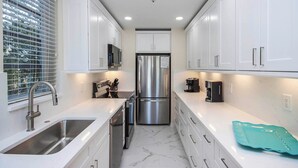 A modern kitchen with white cabinets, stainless steel appliances, and a marble floor.