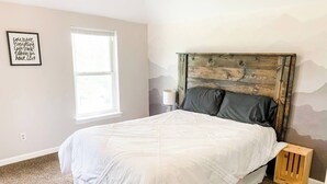 Un dormitorio con una cama grande, cabecera de madera, una ventana y una cita motivacional en la pared.