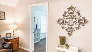 Una sala de estar con un sofá de cuero marrón, una mesa de centro de madera, una consola blanca con un jarrón y plantas, y un adorno de pared.