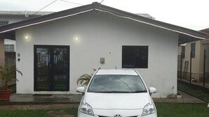 A white car parked in front of a house with a black door and a small window. - Porsche Place in San Fernando (Marabella)