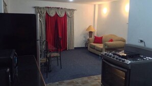 A compact living space with a kitchenette, a sofa, a dining table with chairs, and a TV. - Porsche Place in San Fernando (Marabella)