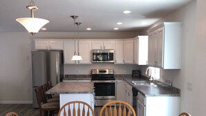 A modern kitchen with white cabinets, stainless steel appliances, and a wooden dining table with chairs. - Beautiful, recently built 6BR/ 4BA Home in Narragansett Pier!!! (Narragansett)