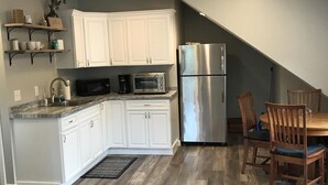 A kitchen with white cabinets, a stainless steel refrigerator, a microwave, and a toaster. There is a dining table with chairs and a rug on the floor. - Beautiful, recently built 6BR/ 4BA Home in Narragansett Pier!!! (Narragansett)
