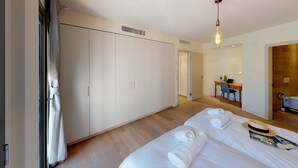 Une chambre d’hôtel avec une grande armoire, un bureau avec un ordinateur portable, un lit avec des serviettes et un chapeau posé sur le lit.