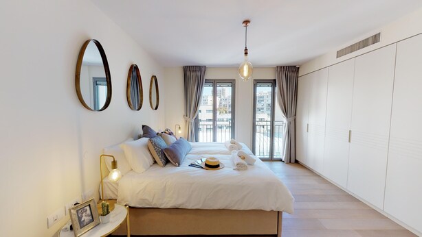 Une chambre à coucher avec un lit, des lampes de chevet, un miroir et une vue sur l’extérieur.
