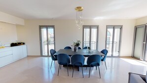Un espace repas moderne avec une table ronde et des chaises bleues, de grandes fenêtres et un luminaire au plafond.