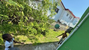 Een groene muur met witte rand, een betonnen trede en een basketbalveldje op de achtergrond.