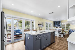 A modern kitchen with a large island, a dining area with a table and chairs, and a view of the outdoors through large sliding glass doors.