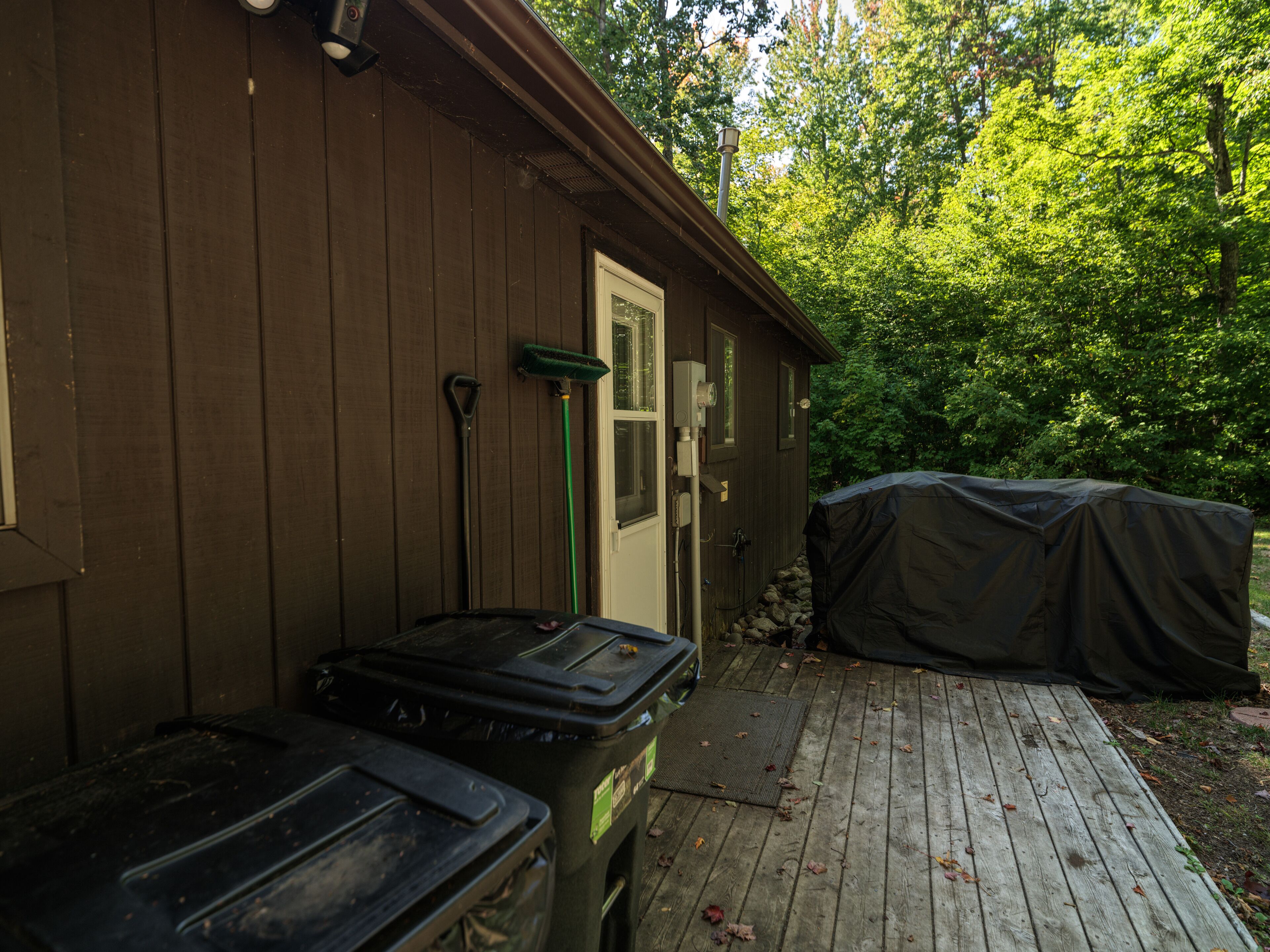 A wooden cabin with a covered outdoor area, a door, and two trash bins.