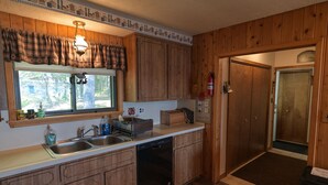 A kitchen with wooden cabinets, a window with a view, a sink, and a fire extinguisher.