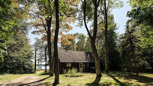 A cabin with a sloped roof, surrounded by tall trees and a grassy area.