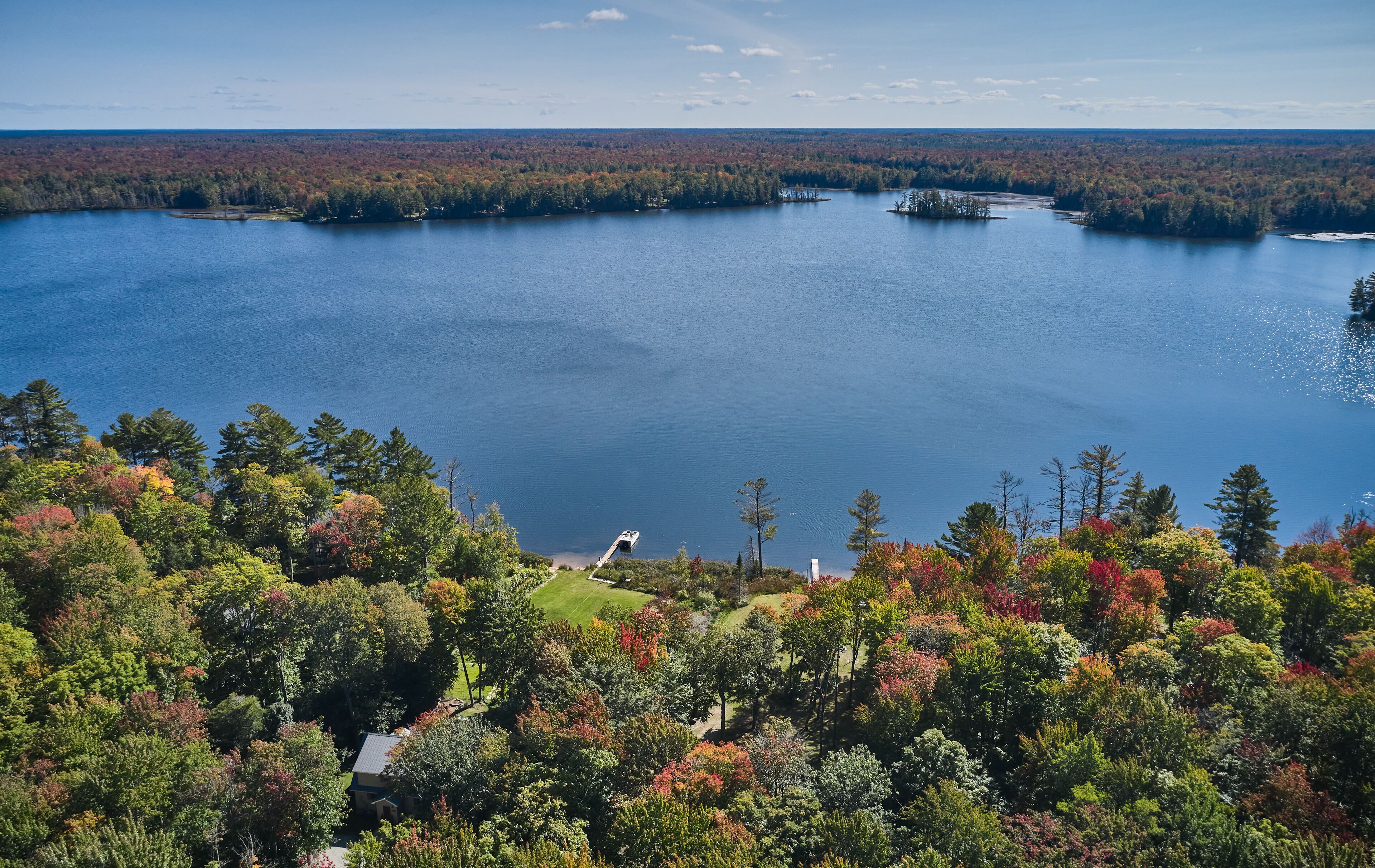 Un lago rodeado de bosque denso, con un pequeño muelle y una casa en primer plano.