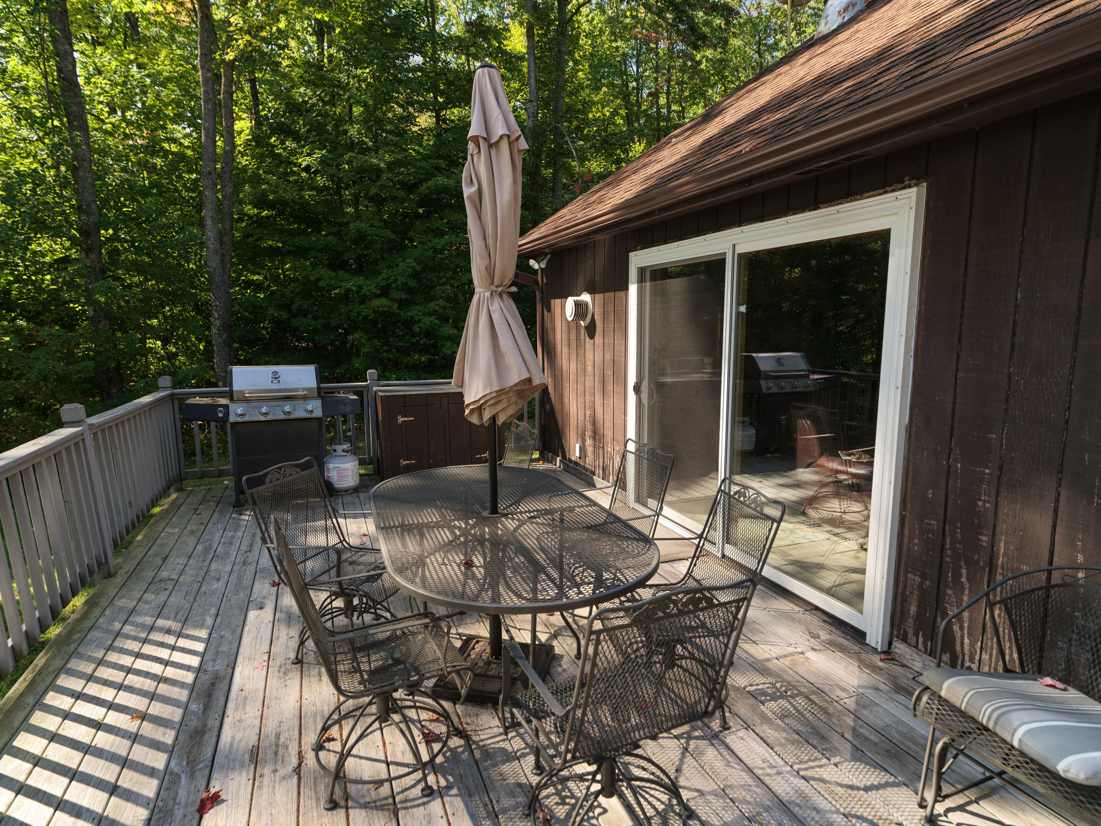 A wooden deck with a round table and chairs, a grill, and a covered umbrella.