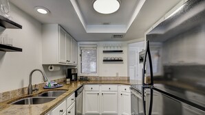A modern kitchen with white cabinets, a stainless steel refrigerator, a coffee machine, and a built-in oven.
