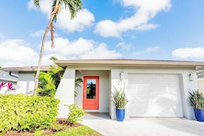 A residential house with a red door, a garage, and a well-maintained front yard with plants. - 529 Whispering Palms Oasis | Private Heated Pool (Naples)