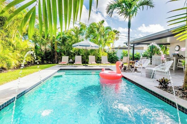 A swimming pool with a pink float, surrounded by palm trees and lounge chairs. - 529 Whispering Palms Oasis | Private Heated Pool (Naples)