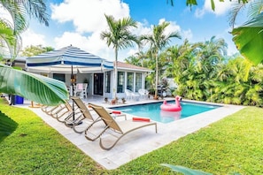 A pool area with lounge chairs, a flamingo float, and a covered seating area with umbrellas.