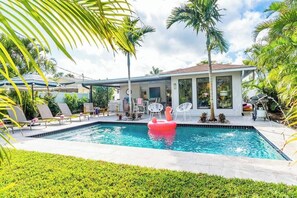A swimming pool with lounge chairs, a flamingo float, and palm trees. - 529 Whispering Palms Oasis | Private Heated Pool (Naples)