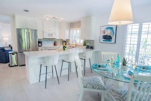 A modern kitchen with white cabinetry, a stainless steel refrigerator, and a glass dining table with blue accents.