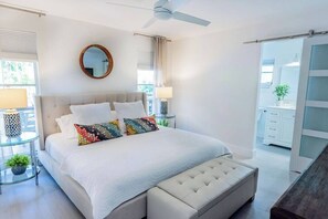 A bedroom with a bed, a round mirror, a ceiling fan, a bedside table with a lamp, and a view of a balcony. - 529 Whispering Palms Oasis | Private Heated Pool (Naples)