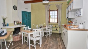 A dining area with a wooden table and white chairs, a window with curtains, and a kitchen area with cabinets and a sink. - Villa al Mare B&B (Giovinazzo)