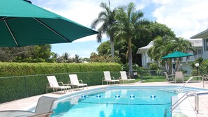A swimming pool with lounge chairs and umbrellas, surrounded by a fence and palm trees.
