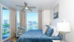 Un dormitorio con una cama grande, un ventilador de techo, vista a la ciudad y un balcón.