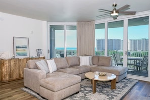 A modern living room with a sectional sofa, a coffee table, and a view of a balcony with outdoor furniture.