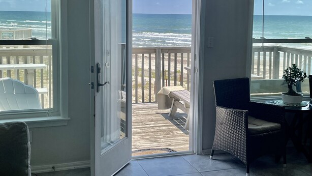 A room with a view of the ocean through an open door, a wicker chair, and a small table with a potted plant. - Beachfront Paradise of Texas 4br 3 1/2 baths (Galveston)