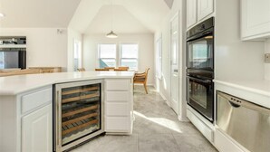 A modern kitchen with white cabinetry, a built-in wine cooler, a stainless steel oven, and a dining area with a table and chairs. - Beachfront Paradise of Texas 4br 3 1/2 baths (Galveston)