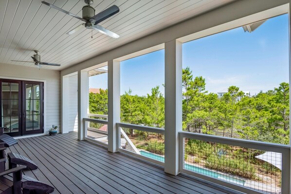 A covered outdoor deck with a ceiling fan, large windows, and a view of a swimming pool and trees. - Seahorse Sunsets-Beach Home w/Large Private Pool, Pet Friendly!South of 30A (Santa Rosa Beach)