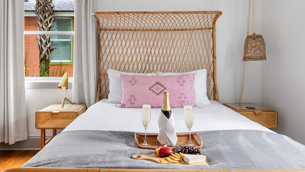 A neatly arranged bedroom with a bed, bedside tables, a wicker headboard, a hanging light, and a window with curtains. - Your Key to Paradise | Southern Shangri-La Suite A (Charleston)