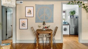 A dining area with a wooden table and chairs, a peace sign tapestry, and a kitchen in the background. - Your Key to Paradise | Southern Shangri-La Suite A (Charleston)