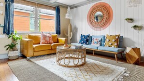 A living room with a yellow sofa, a blue sofa, a round wicker coffee table, and a large mirror with a circular frame. - Your Key to Paradise | Southern Shangri-La Suite A (Charleston)