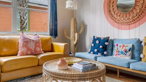 A living room with a yellow sofa, a blue sofa, a round wicker coffee table, and a large mirror on the wall. - Your Key to Paradise | Southern Shangri-La Suite A (Charleston)